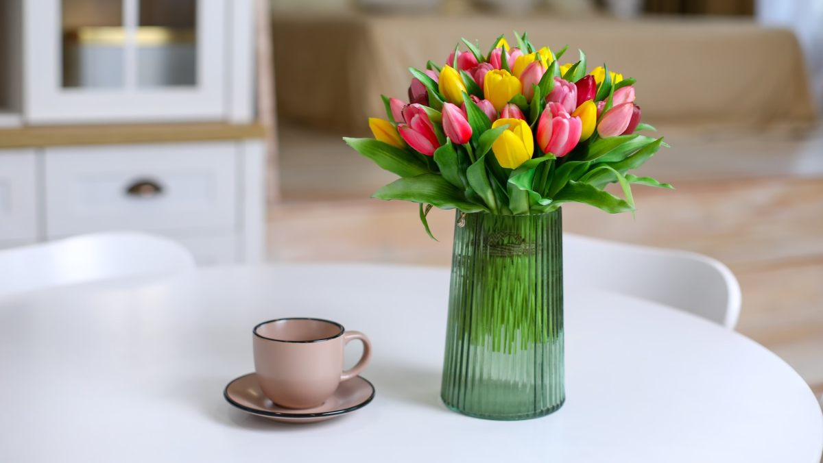 grüne vase mit tulpen neben rosa kaffeetopf