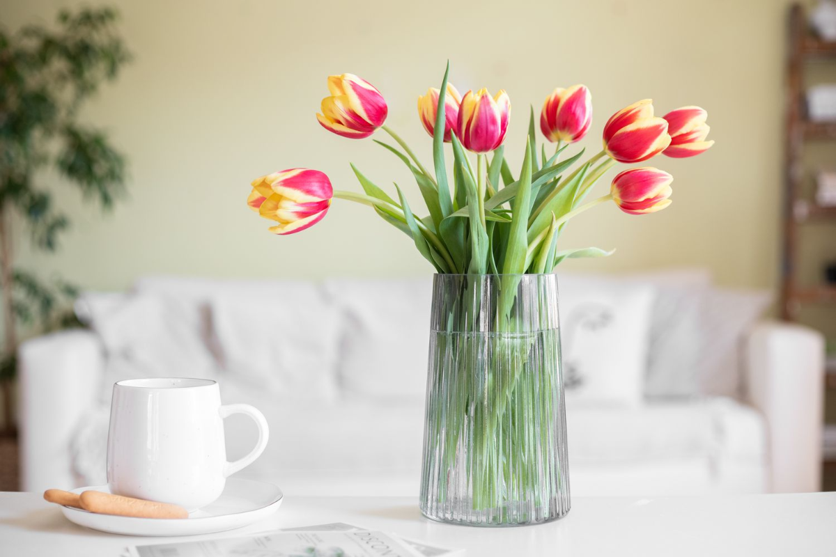 rote und gelbe tulpen in einer glasvase neben einem weissen teeglas