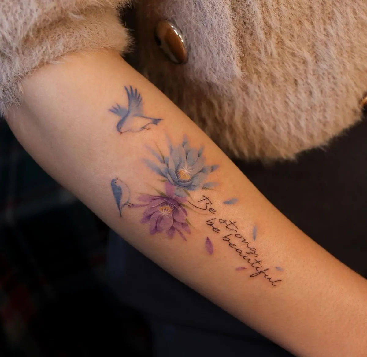be strong be beautiful tattoo am unterarm mit blumen und zwei kleinen vögeln