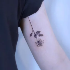 kleines rosen tattoo am oberarm frauen motiv