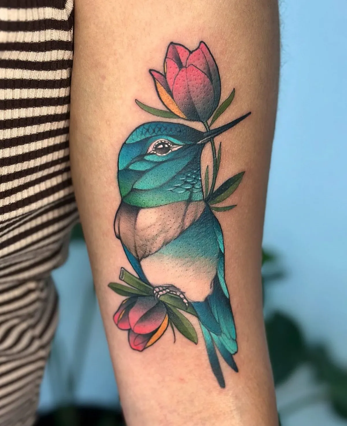 oberarm tattoo bluer kolibri mit zwei roten blumen