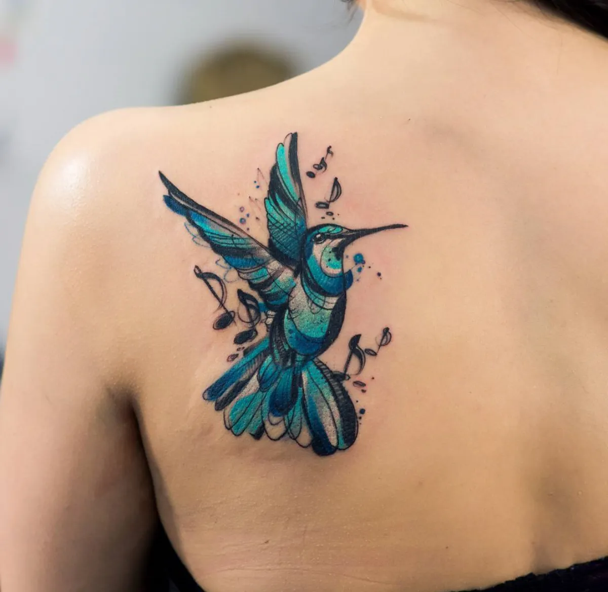 rücken tattoo frau blauer kolibri mit noten