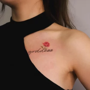 schriftzug tattoo mit kleiner rotoer rose am brust goddess