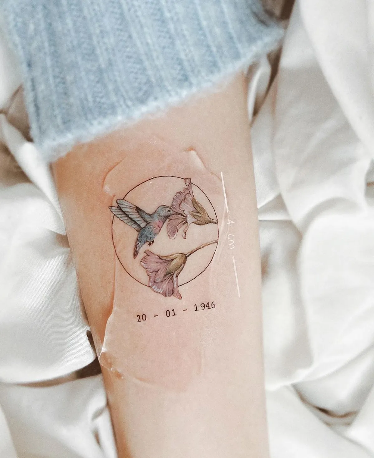 tattoo unterarm kolibri im kreis zwei blüten datum