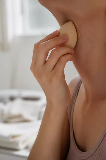Hand tupft mit feuchtem Schwämmchen Foundation an der Kieferlinie aus