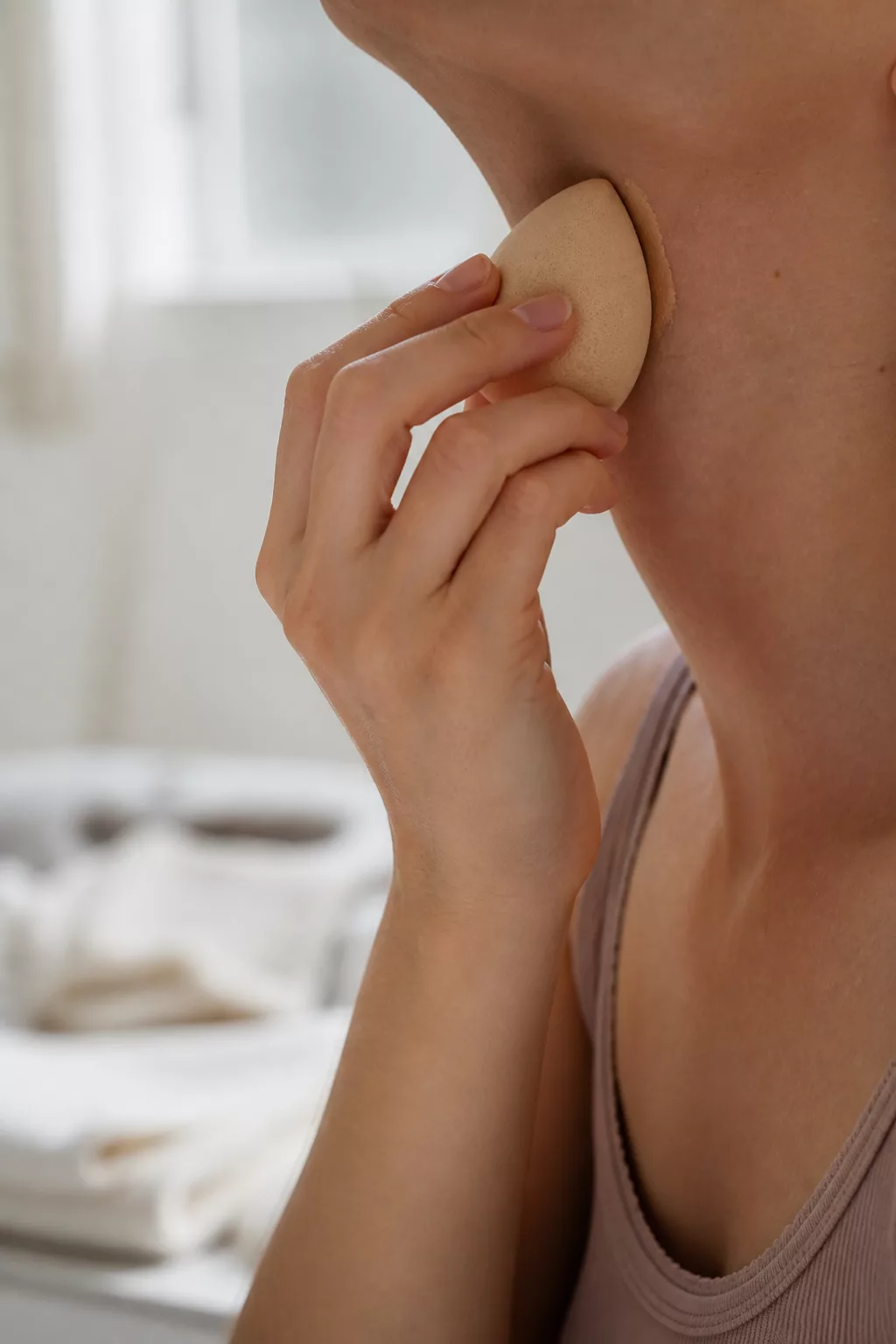 Hand tupft mit feuchtem Schwämmchen Foundation an der Kieferlinie aus