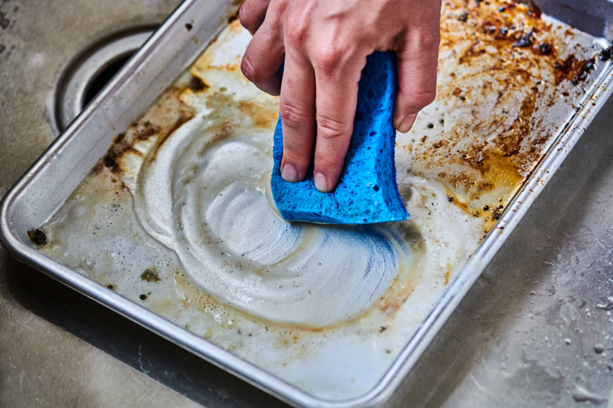 stark verschmutztes backblech mit blauem schwamm reinigen