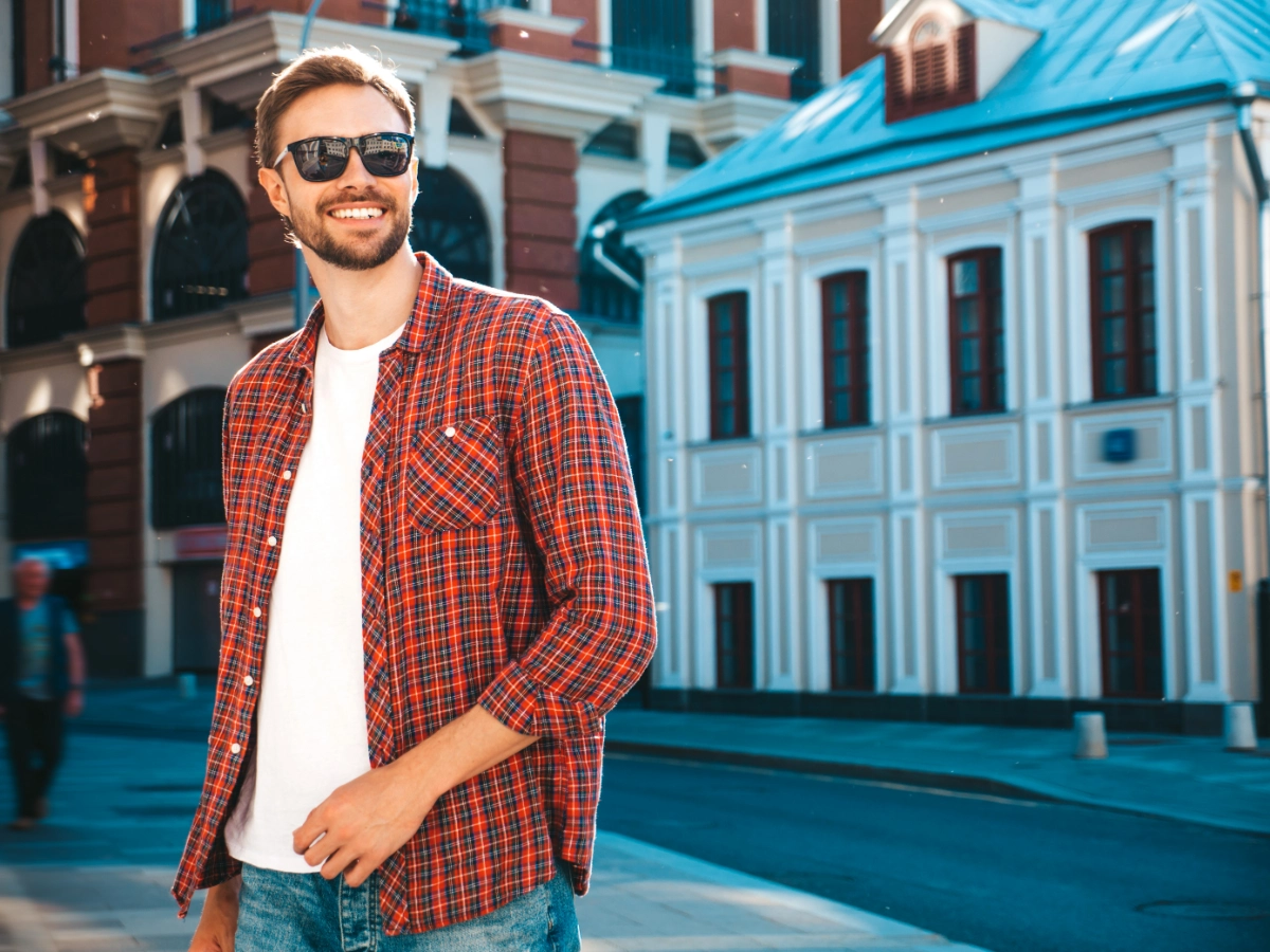 handsome smiling stylish hipster lambersexual model modern man dressed red checkered shirt fashion male posing near skyscraper street background sunglasses outdoors sunset