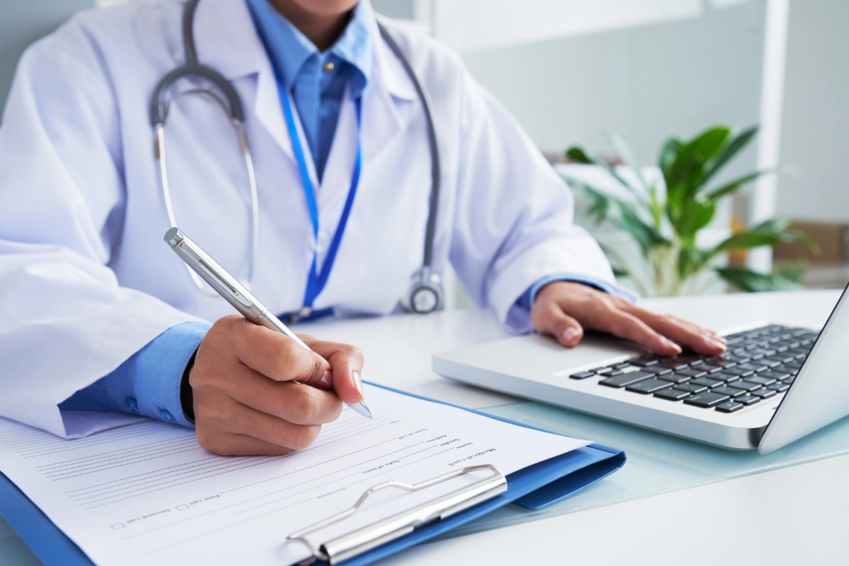 hands unrecognizable female doctor writing form typing laptop keyboard