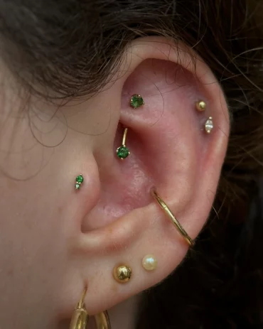 verschiedene bunte piercings und rook piercing mit grünem schmuckstein