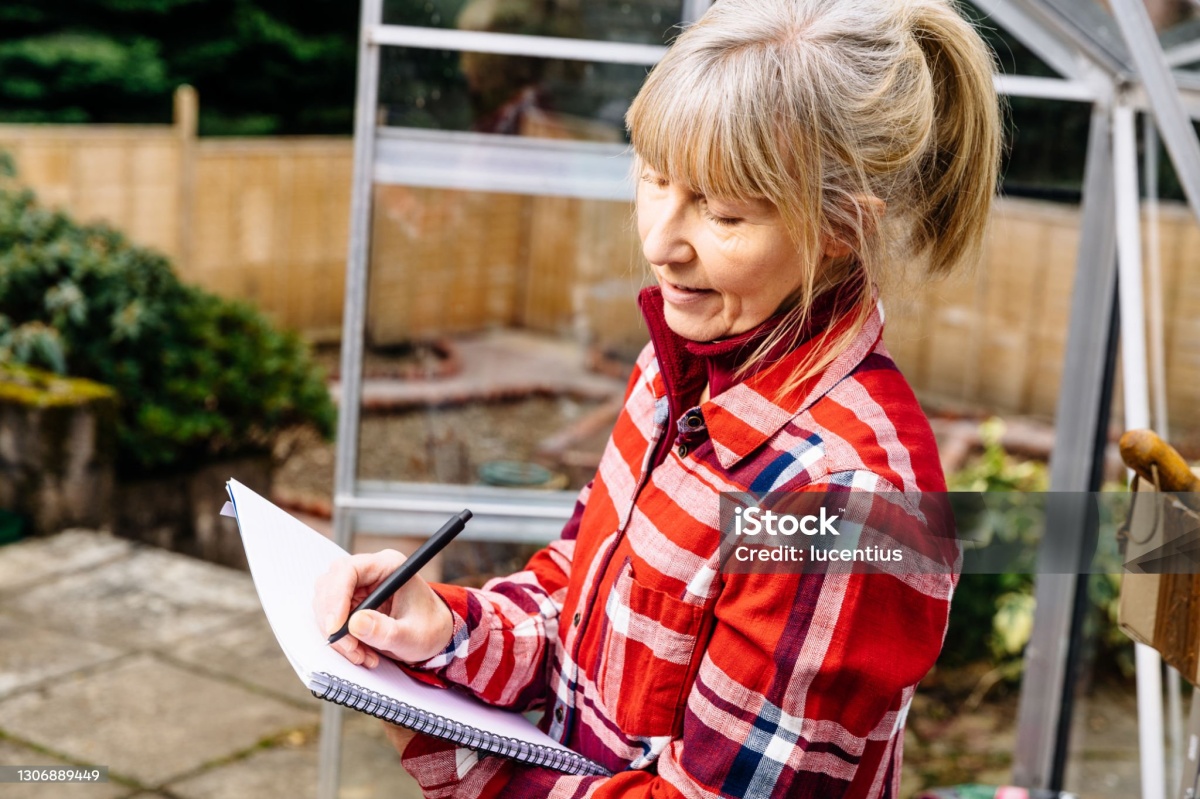 woman in her greenhouse planning the summer ahead with pen and note pad.