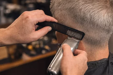 Barbier schneidet mit Kamm und Maschine graues Männerhaar