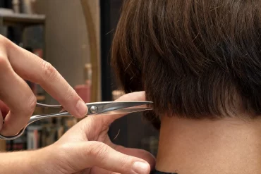 Friseurhände kürzen mit der Schere kurze Haarspitzen im Nacken