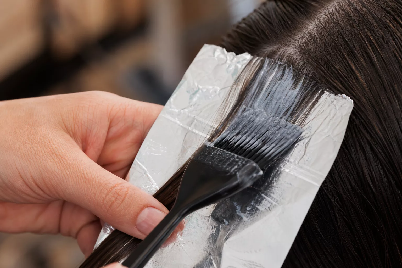 Hand trägt Tönung auf eine braune Haarsträhne auf