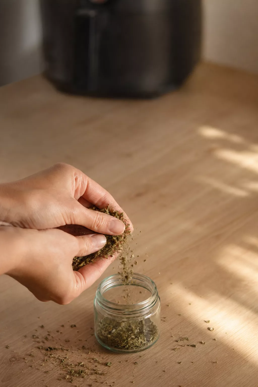 Hände zerbröseln getrocknete Kräuter über einem kleinen Glas