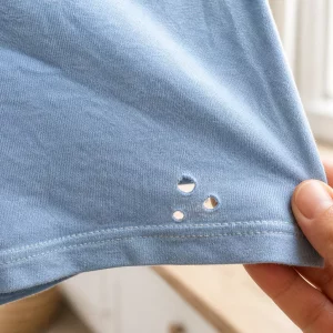 Kleine Löcher in Kleidung nahe dem Saum eines hellblauen Baumwollshirts