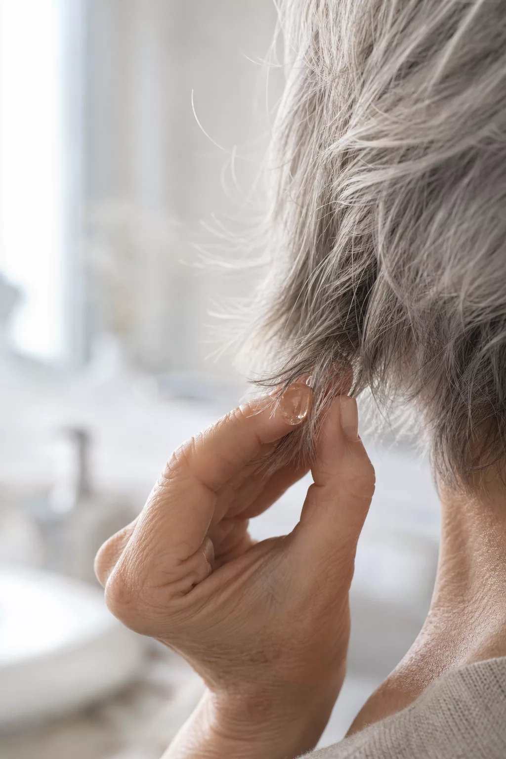 Hand träufelt Haaröl auf silbergraue Spitzen eines Short-Shag-Haarschnitts