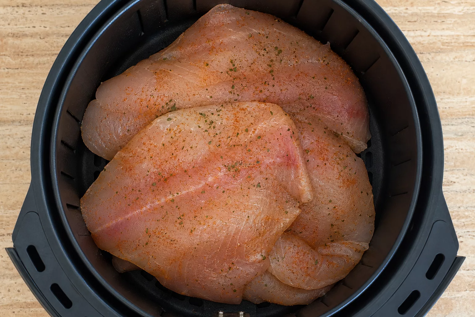 Überfüllter Airfryer-Korb mit übereinanderliegenden Fischfilets