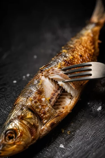 Nahaufnahme einer aufgebrochenen, goldbraun-knusprigen Sardinenhaut