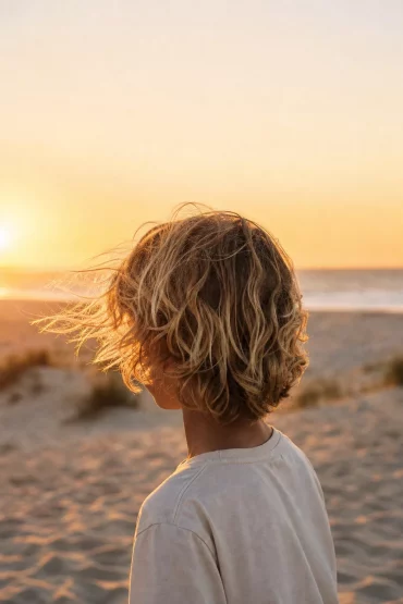 Junge mit sonnengebleichten Locken am Strand von hinten